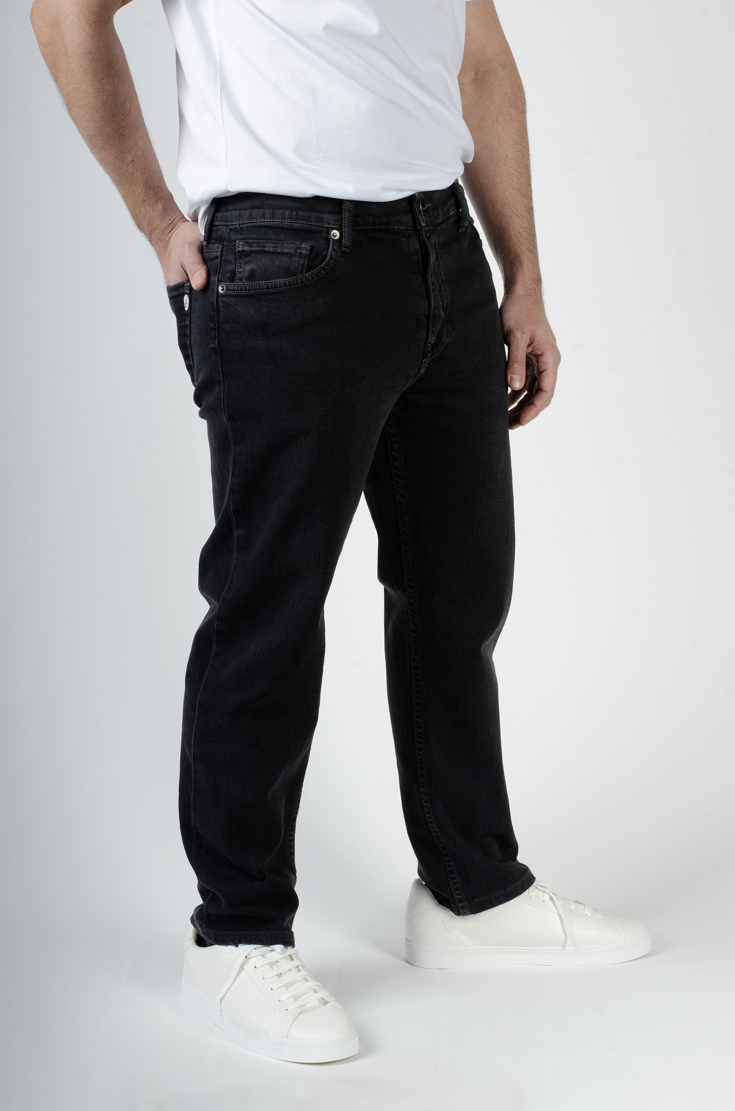 A male model who is 5'6" is wearing charcoal black 5-pocket jeans.. His body is angled to give a front and side view. Classic 3-pocket design in front. His hand is in his back pocket.
